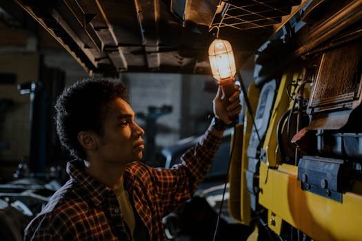 Auto mechanic inspecting a truck engine with a trouble light in a dimly lit garage.